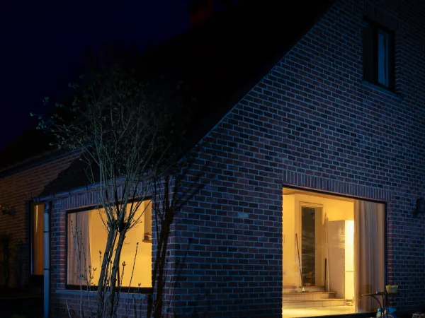 Nieuwe woning van donkere baksteen bij avond, met verlichte ramen