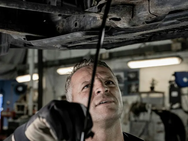 Keurmeester controleert met een lamp de onderkant van een auto op de brug