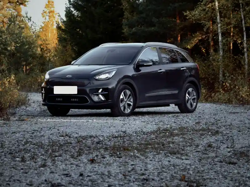 Donkergrijze Kia Niro op een grindpad tussen de bomen