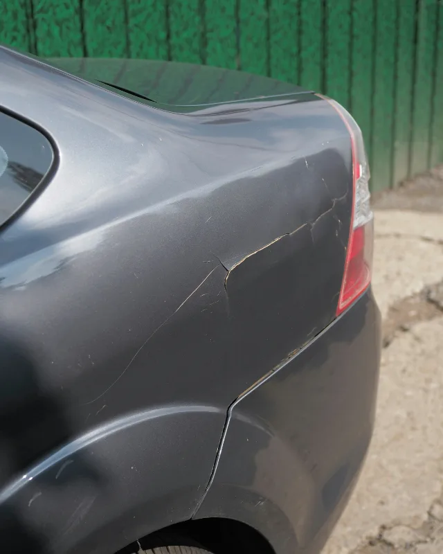 Grijze auto met een gescheurde achterbumper en een barst in de lak boven het wiel