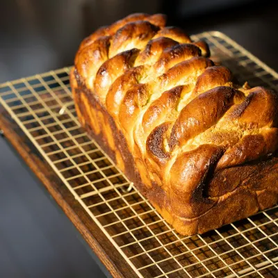 Een gevlochten, glanzend brood op een afkoelrooster