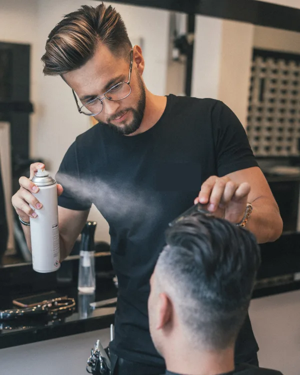 Wybren met bril zet het haar van een klant vast met haarlak
