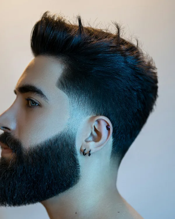 Man van opzij met een hoge fade, opgeborsteld haar en een volle, strakke baard