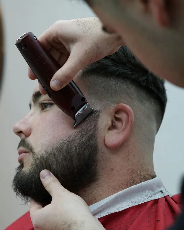 Een barbier zet met de trimmer de lijn van een baard bij de wang