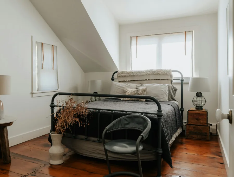 Lichte kamer met een smeedijzeren bed, een stoel en een raam onder een schuin dak