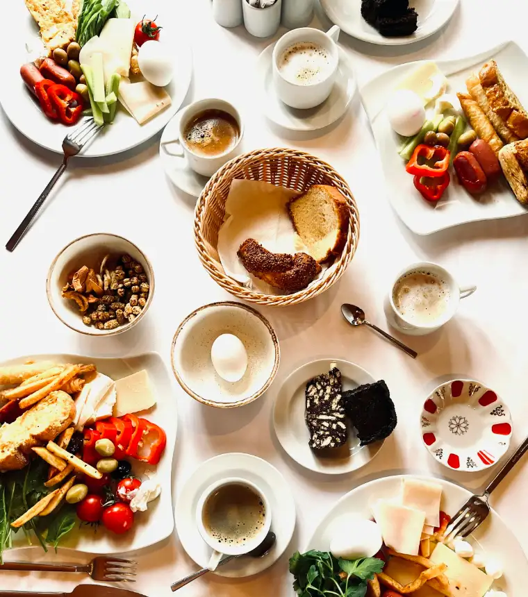 Van bovenaf: een ontbijttafel met brood, eieren, kaas, fruit en koffie