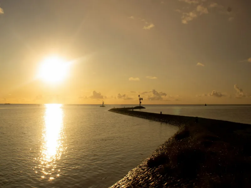 De zon zakt in het water naast een stenen pier
