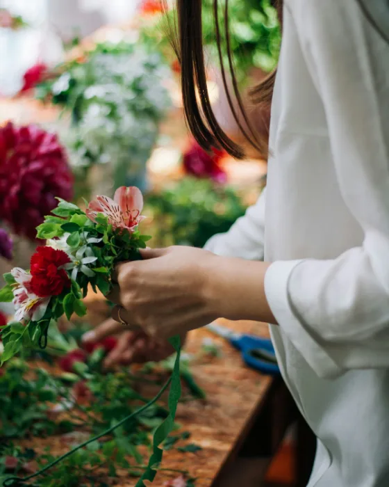 Een bloemist bindt een boeket met rode en roze bloemen aan een werktafel