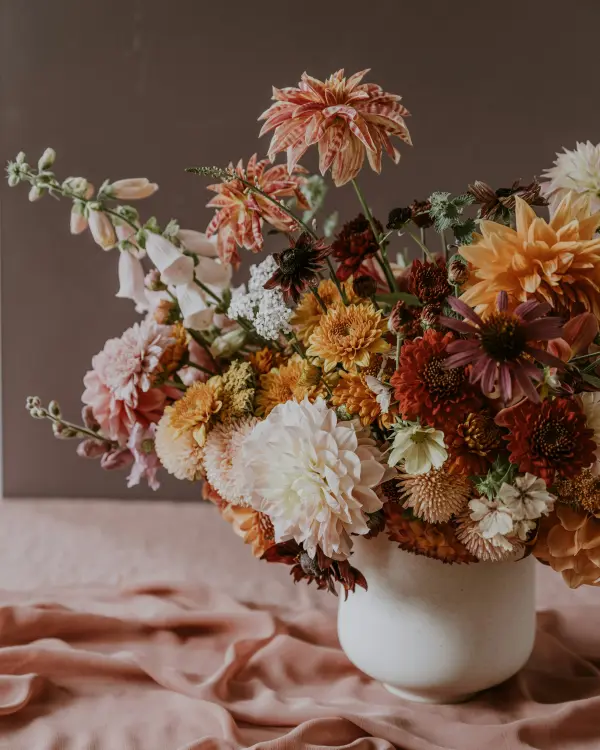Een volle herfstschikking met dahlia's en chrysanten in een witte kruik