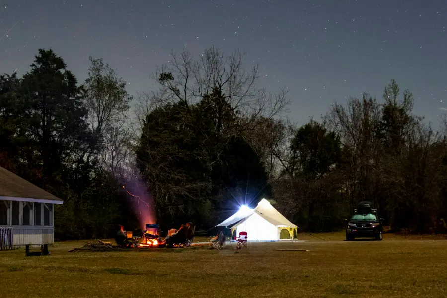 Een kampvuur en een verlichte tent op een grasveld in de avond