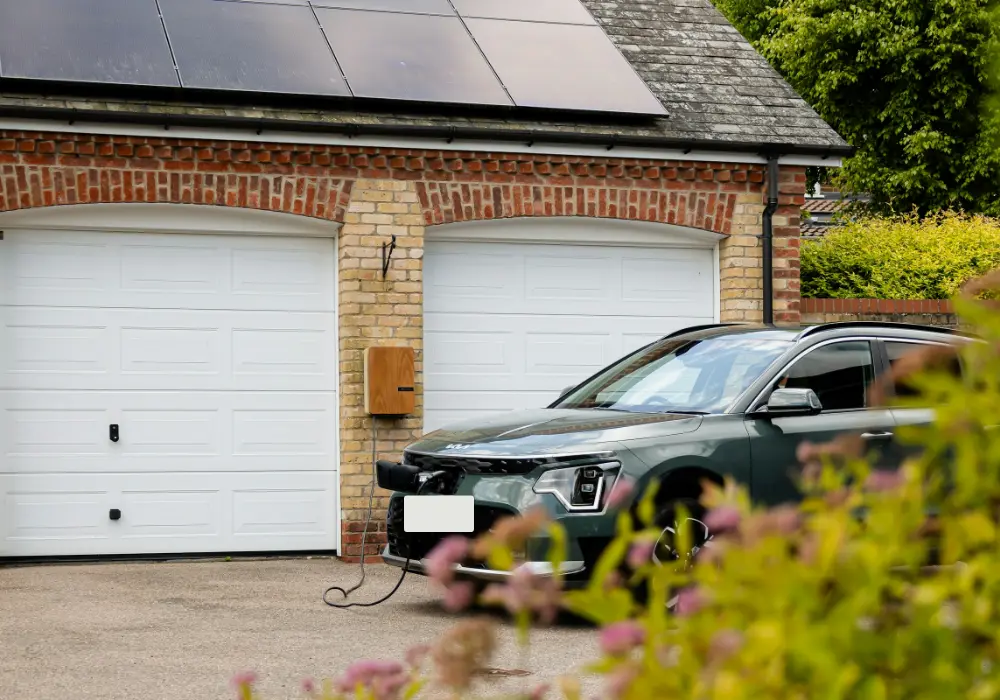 Groene elektrische auto aan de laadkabel voor een dubbele garage met zonnepanelen op het dak