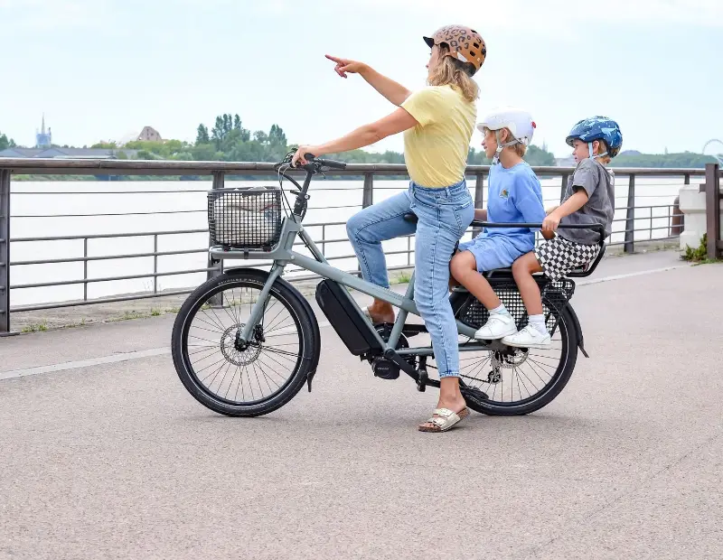 Een moeder op een lange e-bike met twee kinderen achterop wijst naar het water