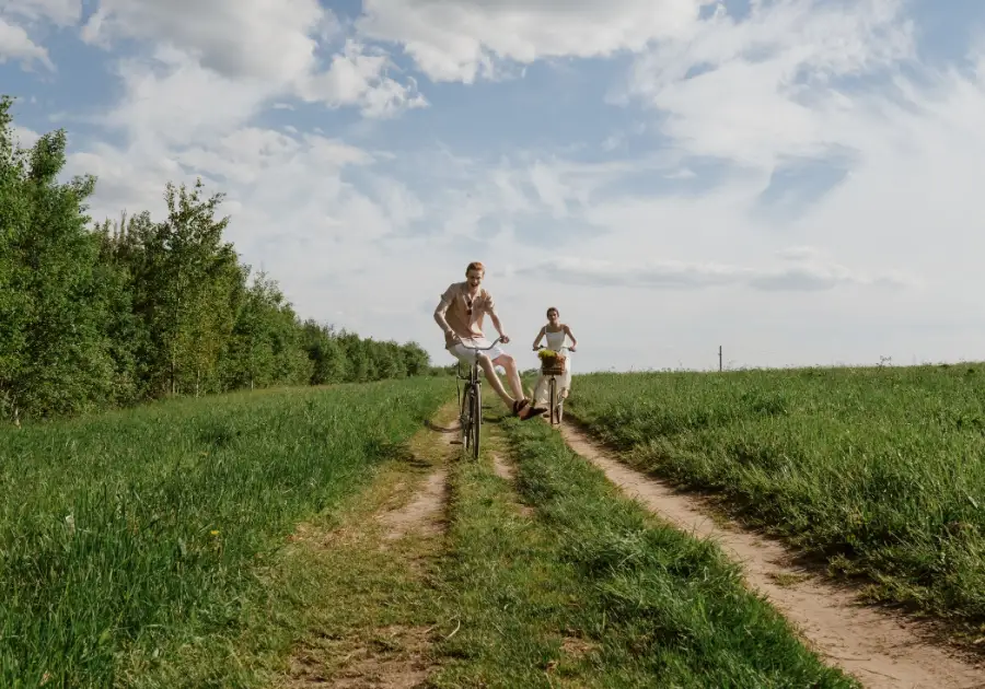 Twee mensen fietsen over een graspad tussen weilanden onder een wolkenlucht