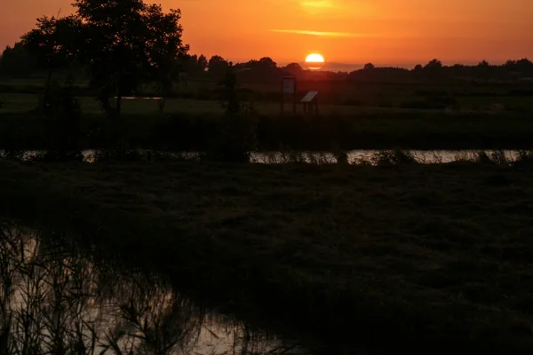 Oranje zonsondergang boven een vlak land met water en bomen