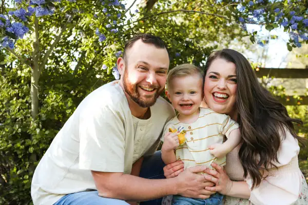Lachende ouders met hun peuter op schoot onder een boom