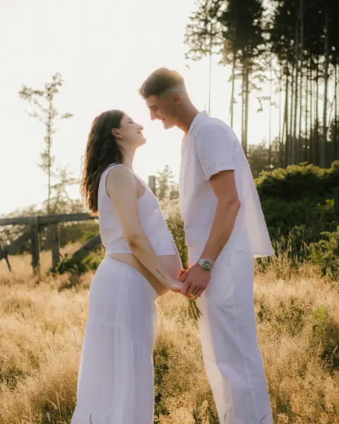 Stel in witte kleding staat hand in hand in een veld met hoog gras