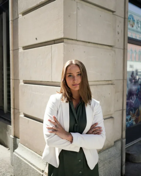 Zakelijk portret van een vrouw met gekruiste armen in een wit jasje voor een stenen gevel
