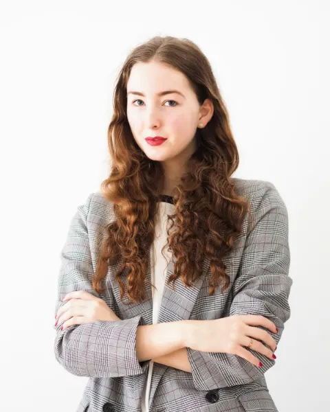 Portret van een jonge vrouw met lang krullend haar in een geruit colbert tegen een witte achtergrond