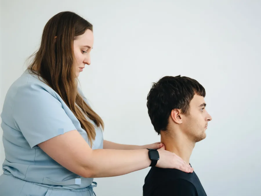 Een fysiotherapeut onderzoekt met haar handen de nek van een man die op een kruk zit
