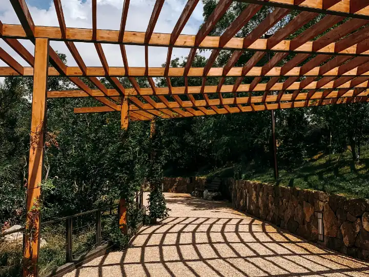 Na: houten pergola over een grindpad, met een stapelmuur van natuursteen en groen erlangs