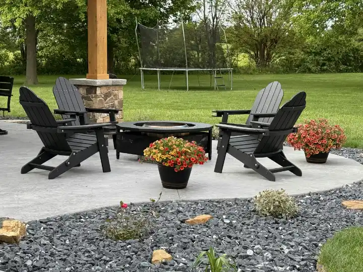 Terras met houten tuinstoelen rond een vuurkorf en een trampoline op het gazon erachter