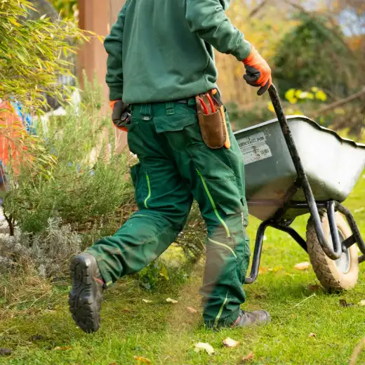 Twee hoveniers in groene werkkleding aan het werk in een tuin, een van hen met een kruiwagen