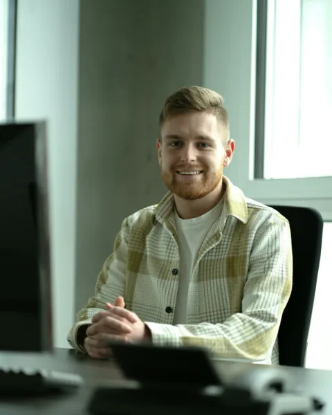 Jelle zit lachend aan een bureau in een licht kantoor, met zijn handen gevouwen