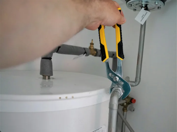 Monteur draait met een waterpomptang een koppeling op een boiler vast