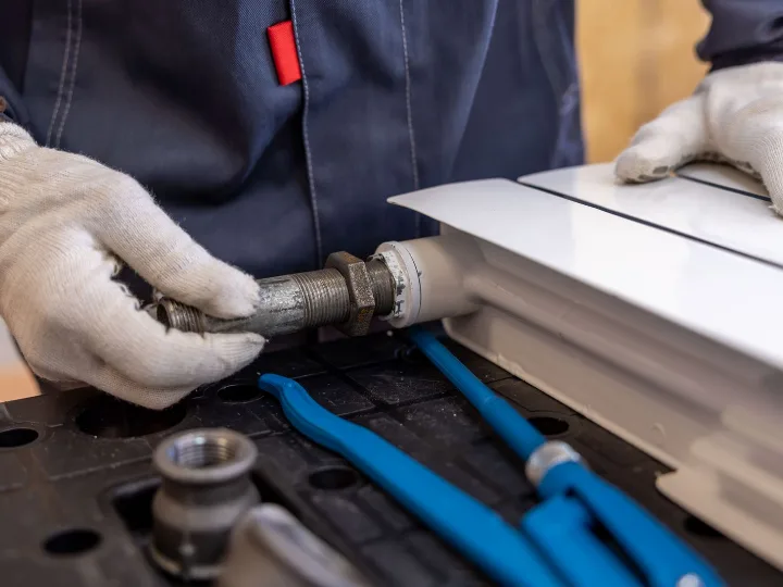 Monteur met werkhandschoenen schroeft een koppelstuk in een nieuwe radiator