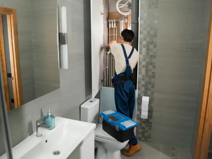 Loodgieter in overall werkt aan de leidingen in een badkamer met wastafel en toilet