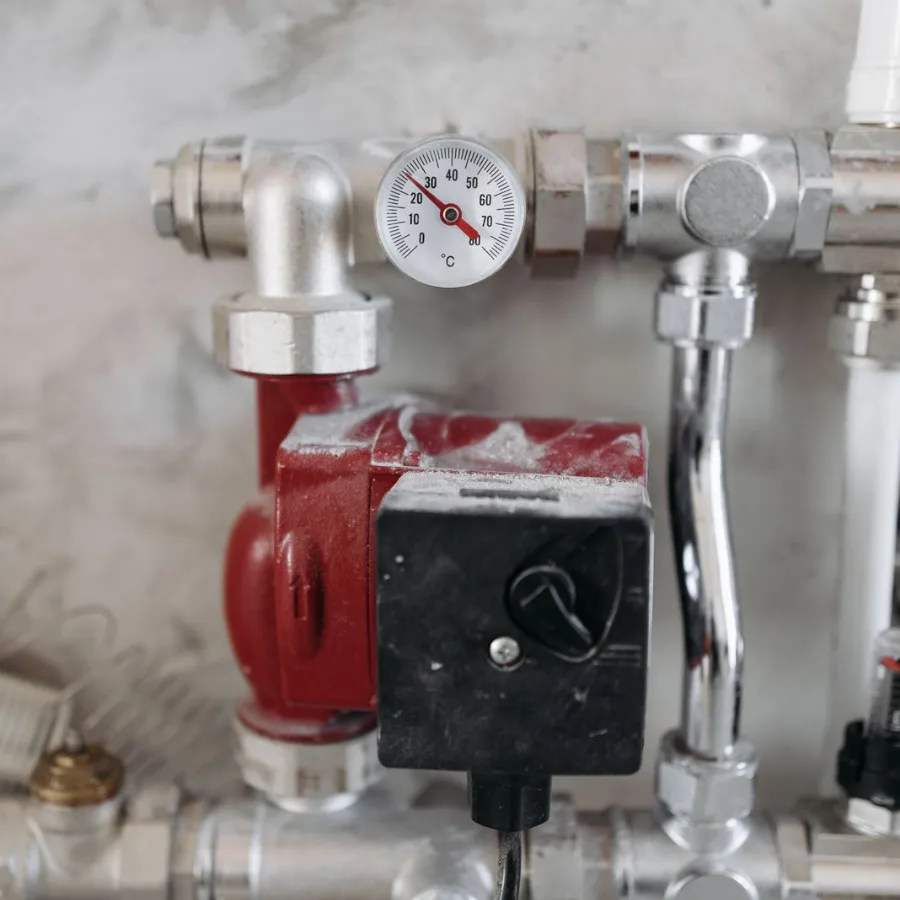 Verdeler van vloerverwarming met een thermometer, een rode circulatiepomp en verchroomde leidingen