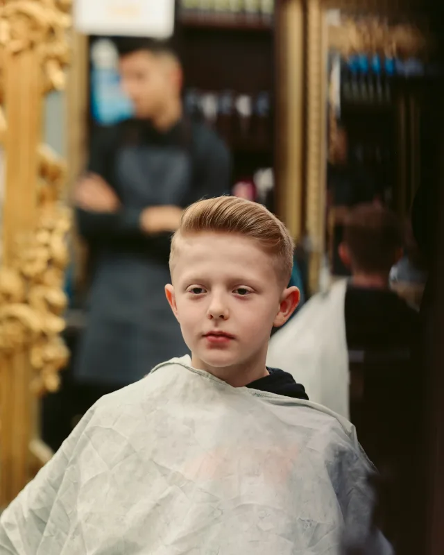 Een jongen met een kapmantel om zit in de kappersstoel