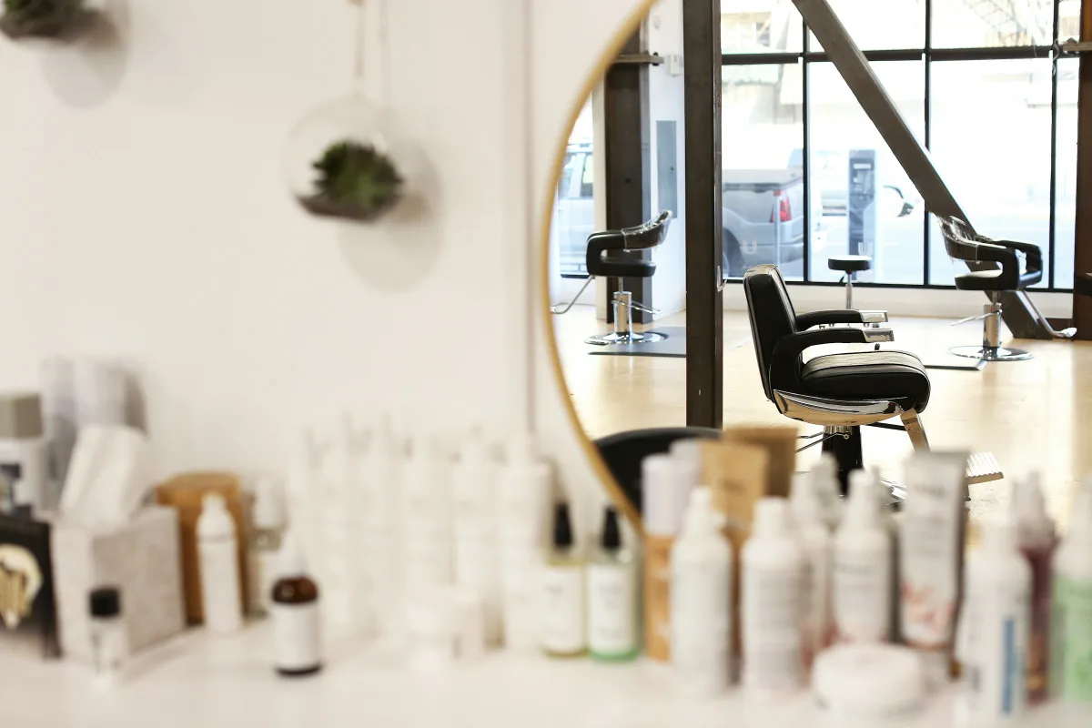 Lichte salon met een ronde spiegel, kappersstoelen en planken vol verzorgingsproducten
