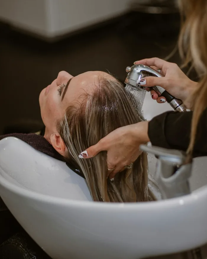 Een klant ontspant bij de wasbak terwijl haar haar wordt gewassen
