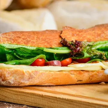 Stokbrood met kaas, komkommer en tomaat op een houten plank