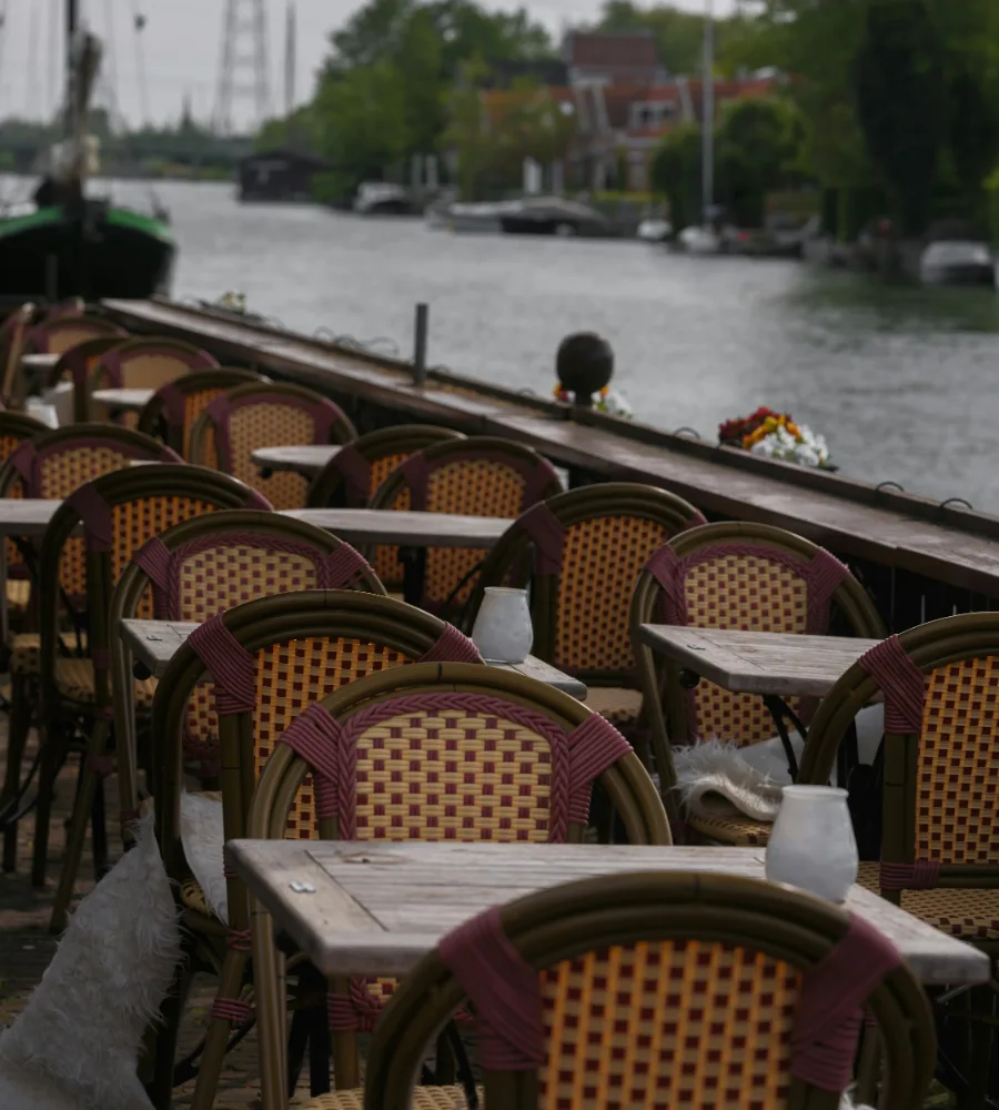 Terras aan het water met rieten stoelen en houten tafeltjes