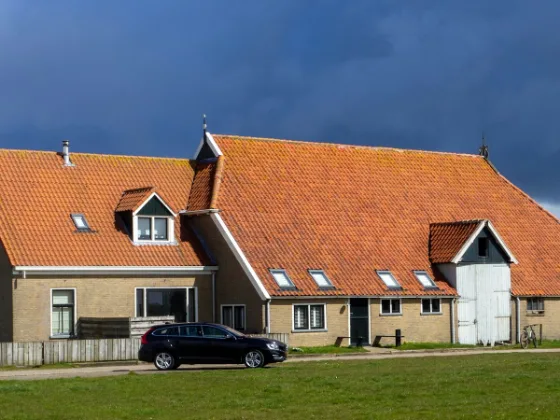 Friese boerderij met een groot oranje pannendak en een witte schuurdeur onder een donkere lucht