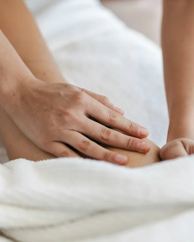 Handen masseren de bovenbeenspier van iemand die onder een witte handdoek ligt