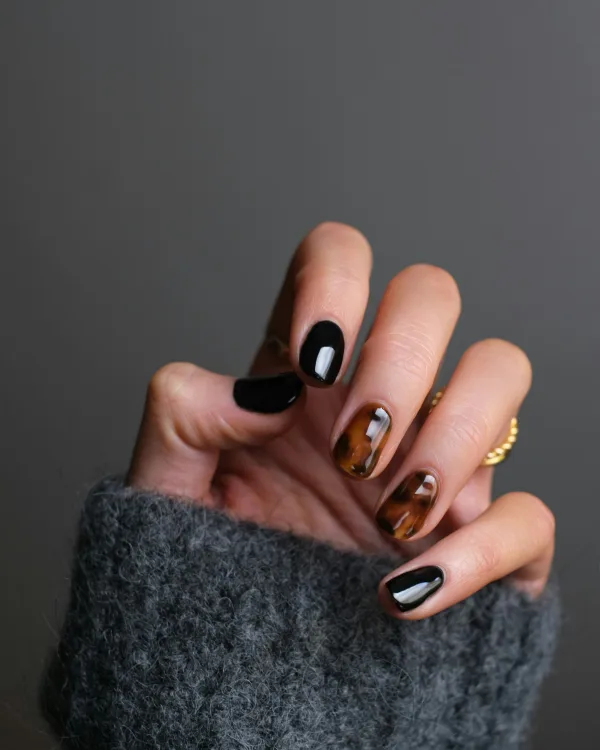 Hand in een grijze trui met zwarte nagels en twee nagels in schildpadprint