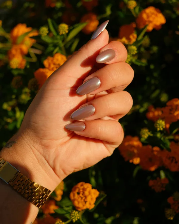 Hand met glanzende taupe amandelnagels voor oranje herfstbloemen