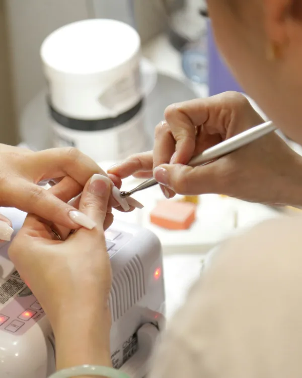 De styliste werkt de nagelriemen bij naast de lamp waarin de gel uithardt
