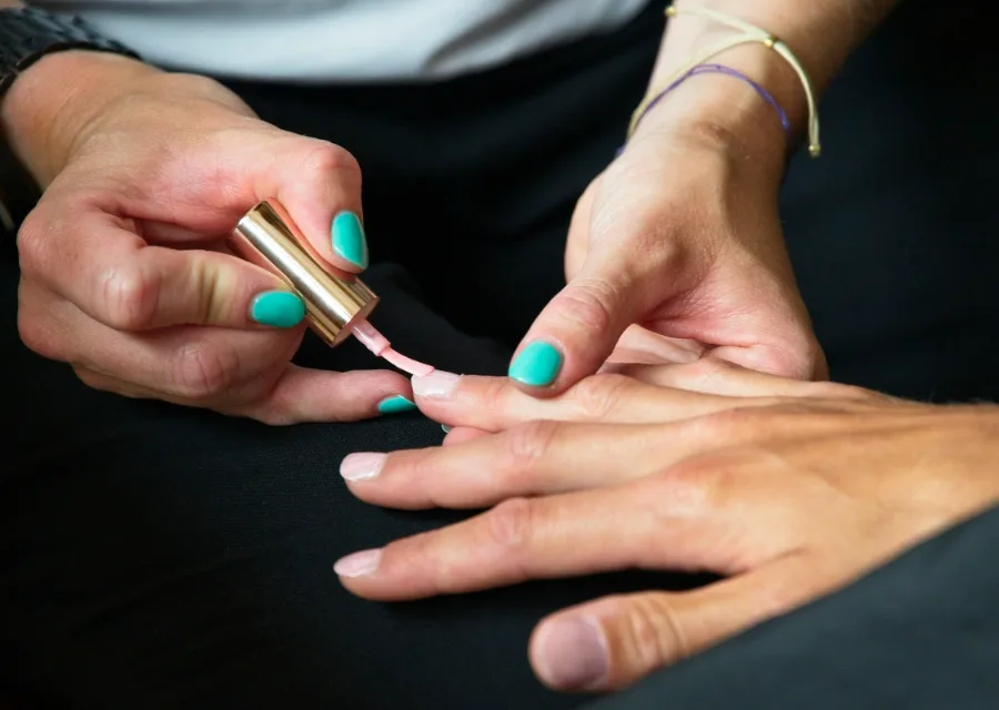 Een nagelstyliste lakt de nagels van een klant met mintgroene lak