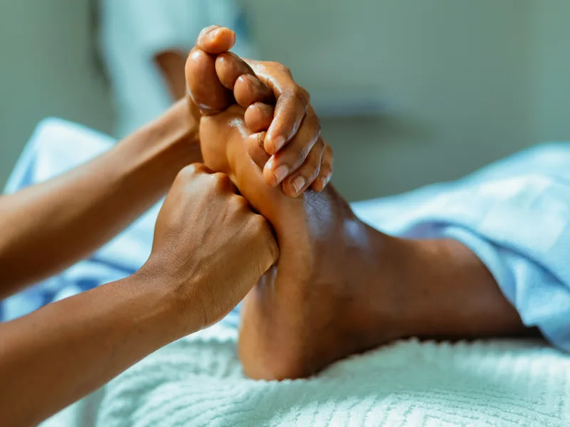 Handen houden de voet van een klant vast die ontspannen op een lichtblauw laken ligt