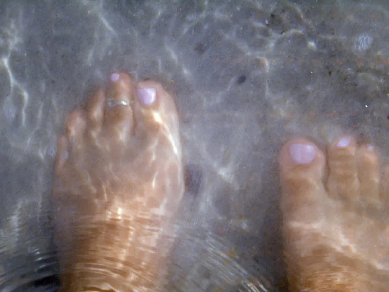 Twee voeten met lichtlila gelakte nagels in een voetbad met helder water