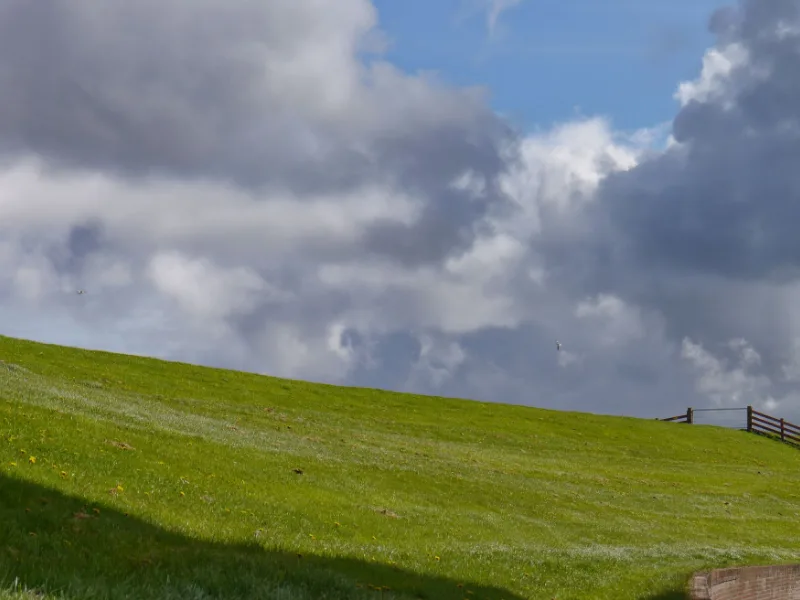 Een groene dijk met gras onder een lucht vol wolken