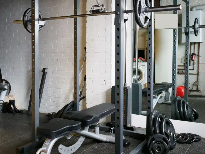 Een kleine trainingsstudio met een rek, halterbank en gewichten tegen een witte muur