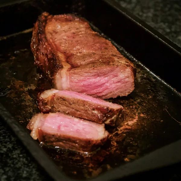 Gegrilde rib-eye, aangesneden, met een roze kern op een zwarte schaal