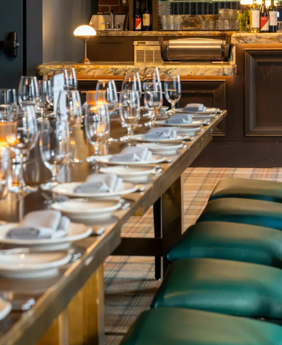 Een lange gedekte tafel met wijnglazen en servetten in een warm verlichte zaal