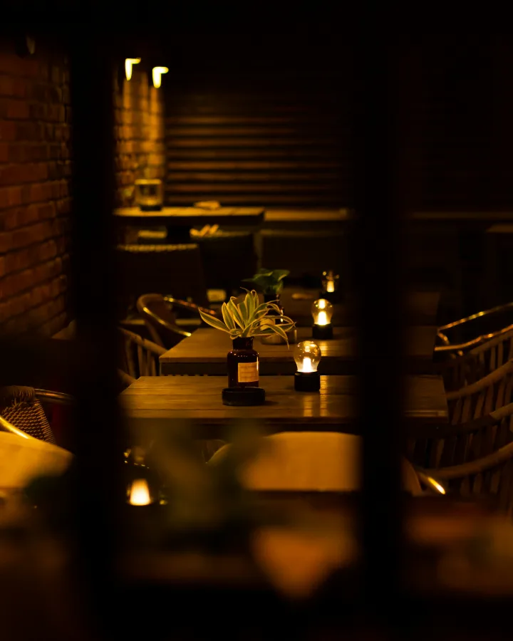De zaal 's avonds: houten tafels met kaarsjes en warm licht tussen donkere wanden