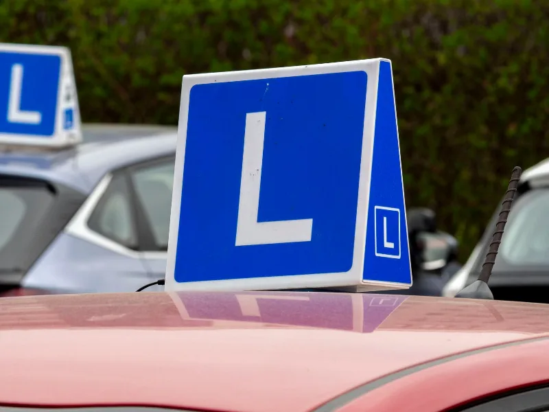 Een blauw bord met een witte L op het dak van een lesauto